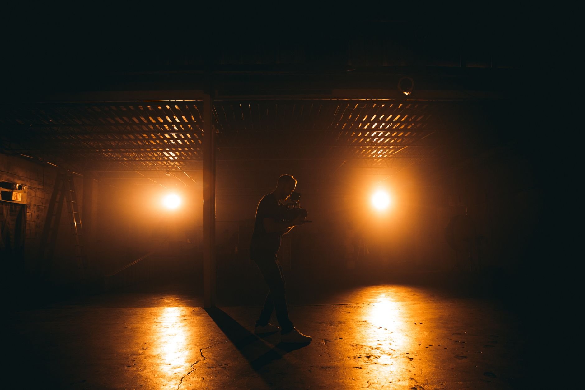 A silhouetted man filming with professional equipment under dramatic lighting in a dim setting.